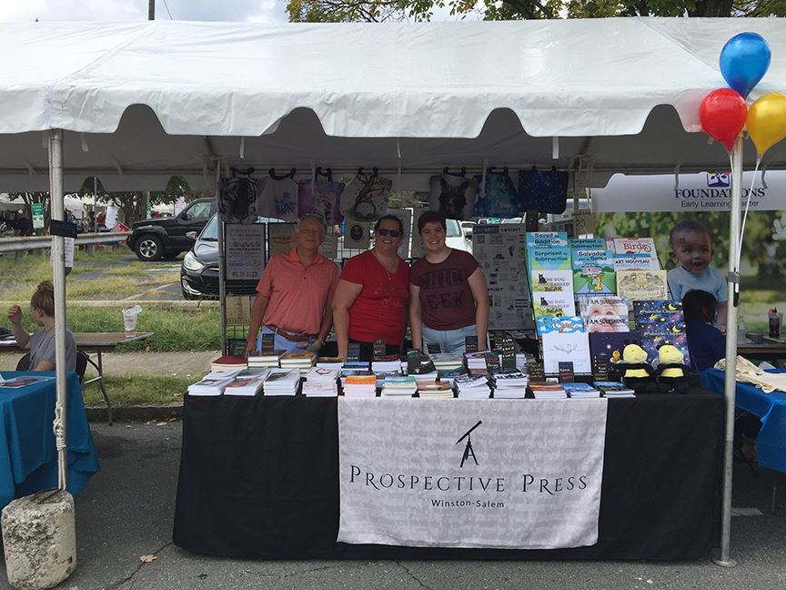 Three authors under a tent with a table of books
